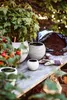 A collection of planters and potting soil arranged on a wooden table, with lush greenery in the background. Produktbild-Vorschau