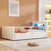 A modern beige upholstered daybed with storage drawers and an LED-lit headboard shelf, set in a minimalist room with a pale orange wall and a patterned rug. Produktbild-Vorschau