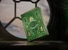 A green and gold deck of Wicked playing cards is displayed in a dimly lit, circular window frame. Náhled obrázku produktu