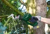 A person's hand wearing a glove is holding a cordless reciprocating saw and cutting a tree branch. Produktbild-Vorschau