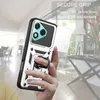 A hand holding a silver and black phone case with a ring holder and a sliding camera cover, with a blurred indoor background. Produktbild-Vorschau