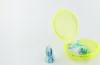 A pair of earplugs in a yellow plastic case, with one earplug outside the case. Produktbild-Vorschau