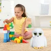 A young girl plays with building blocks next to a stuffed owl toy in a room. Produktbild-Vorschau