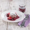 A chocolate dessert with berries and powdered sugar on a wooden table, with a small jar of berry sauce. Náhled obrázku produktu