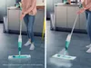 A person is cleaning a floor with a spray mop in a kitchen setting. Produktbild-Vorschau