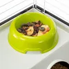 A close-up of a green pet food bowl filled with dry food and dried fruit pieces, placed on a white textured surface within a cage. Podgląd zdjęcia produktu