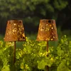 Two solar garden lights with a floral cut-out design are placed in lush green foliage. Produktbild-Vorschau