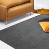 A close-up view of a gray rug in a living room setting, with a brown sofa and orange and black pillows visible. Anteprima dell’immagine prodotto