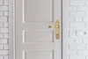 A close-up view of a white door with a gold door handle, set against a white brick wall. Anteprima dell’immagine prodotto