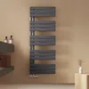 A modern anthracite towel radiator mounted on a light brown wall, with a shelf and soap dispensers to the left, and a small decorative plant on a wooden cube to the right. Náhled obrázku produktu