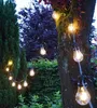 String lights with Edison-style bulbs are strung around a tree in a garden at dusk. Produktbild-Vorschau
