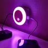 A purple LED night light with a circular white light ring is plugged into a wall socket. Two USB cables extend from the night light, one connecting to a black electronic device and the other to a smartphone. Produktbild-Vorschau