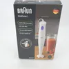 The image shows the packaging of a Braun MultiQuick 1 hand blender. The packaging is mostly dark gray with white text and graphics. A white hand blender with a blue button is depicted on the right side of the box, along with a glass of smoothie and a tomat Náhled obrázku produktu