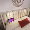 A bed with a tufted headboard, a tablet displaying the word 'mini' with colorful text, and a red pillow. Náhled obrázku produktu