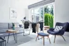 A drying rack with clothes is placed in a modern living room with a sofa, armchair, and a large window overlooking a garden. Produktbild-Vorschau
