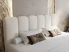 A close-up view of a bed with a white upholstered headboard and pillows. Produktbild-Vorschau