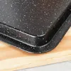 A close-up view of a speckled black baking tray with raised edges, resting on a light wooden surface. Náhľad obrázku produktu