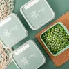 Three green storage containers with white lids are arranged on a green surface, with one container filled with frozen peas. Náhľad obrázku produktu
