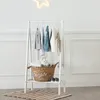 A white wooden children's wardrobe with clothes hanging on it and a basket with a stuffed animal on the shelf below. Produktbild-Vorschau