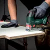 A person wearing work gloves is using a Metabo jigsaw to cut a piece of white material on a table. Podgląd zdjęcia produktu