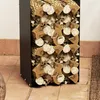 A black metal firewood rack filled with logs, placed on a tiled floor next to a white wall. Produktbild-Vorschau