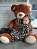 A young girl hugging a large teddy bear in a room with a dresser and shelves. Podgląd zdjęcia produktu