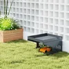 A robotic lawn mower shelter is placed on a grassy lawn next to a planter with plants and a white lattice wall. Produktbild-Vorschau