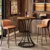 A bar table and two stools are set up in a room with a brick wall and a bar cabinet in the background. Produktbild-Vorschau
