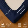 A close-up of a navy blue fitted sheet corner, showing the elasticized edge and some product feature icons at the bottom. Produktbild-Vorschau