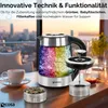 A glass electric kettle with colorful LED lighting is shown on a table with a cup of tea and a tea infuser, with a city skyline visible through a window in the background. Produktbild-Vorschau
