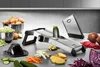 A kitchen counter with a mandoline slicer, various vegetables, and bowls of chopped vegetables. Podgląd zdjęcia produktu