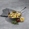 A stainless steel frying pan filled with pasta, cherry tomatoes, and spinach, placed on a gray surface next to a folded gray napkin, a whole tomato, some spinach leaves, and a nest of uncooked pasta. Podgląd zdjęcia produktu