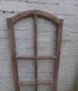 A wooden window frame with arched top and multiple panes, leaning against a brick wall. Produktbild-Vorschau