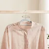 A light pink button-up shirt is hanging on a gray hanger on a wooden rack. Náhled obrázku produktu