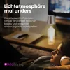 A person is relaxing on a couch with headphones on, while a bottle lamp is lit on a table in the background. Anteprima dell’immagine prodotto