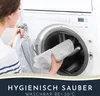 A woman is putting a bath mat into a washing machine. Anteprima dell’immagine prodotto