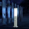 A modern stainless steel bollard light with a motion sensor stands on a lawn in front of a wooden fence at night. Voir les images du produit