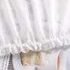 A close-up view of a white sheer curtain with ruffles at the bottom, partially obscuring a slice of cake. Produktbild-Vorschau