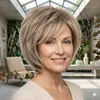 Frau trägt eine kurze, geschichtete blonde Bob-Perücke mit seitlich gefegtem Pony, lächelt in einem modernen Raum mit Pflanzen Voir les images du produit