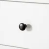 A close-up of a black drawer knob on a white surface. Produktbild-Vorschau