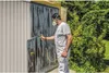 A man wearing a mask and white overalls is spray painting a garage door with a paint sprayer. Produktbild-Vorschau