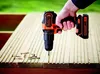 A hand is holding a Black & Decker cordless drill and screwing a screw into a wooden deck. Anteprima dell’immagine prodotto
