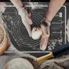 Hands in gloves are preparing dough on a baking mat with measurement markings. A rolling pin and a bowl are also visible. Voir les images du produit