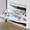 A close-up view of a white shoe cabinet with two shelves, displaying a pair of gray sneakers on the bottom shelf and a pair of brown slip-on shoes on the top shelf. Podgląd zdjęcia produktu
