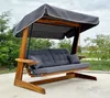 An outdoor swing set with a canopy and cushions, placed on a paved surface with greenery in the background. Podgląd zdjęcia produktu
