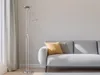 A floor lamp with two lights stands next to a sofa in a living room. Náhled obrázku produktu