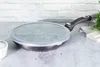 A frying pan with a glass lid sits on a countertop in front of a brick wall. Podgląd zdjęcia produktu