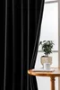 A black curtain is partially drawn, revealing a window with a potted plant and a book on a small wooden table. Produktbild-Vorschau