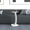 A white C-shaped side table with a cup and a remote on top, placed next to a dark gray sofa. Podgląd zdjęcia produktu