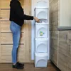 A person is shown using a stackable trash can system in a room with wooden doors and cabinets. Náhled obrázku produktu